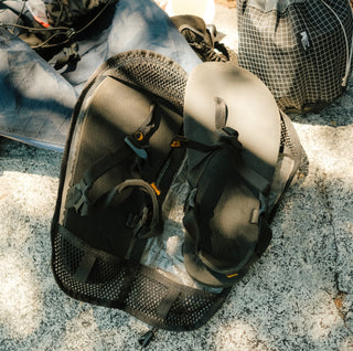Pair of black sandals held within a unique fitted bag with mesh design laying on a rock